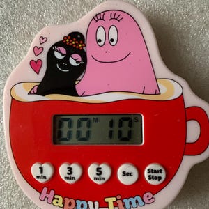Pode incluir: Um temporizador de cozinha rosa e vermelho em forma de chávena, com personagens de desenhos animados. O temporizador mostra "00:10" e tem botões para minutos e segundos. As palavras "Happy Time" estão impressas na parte inferior.