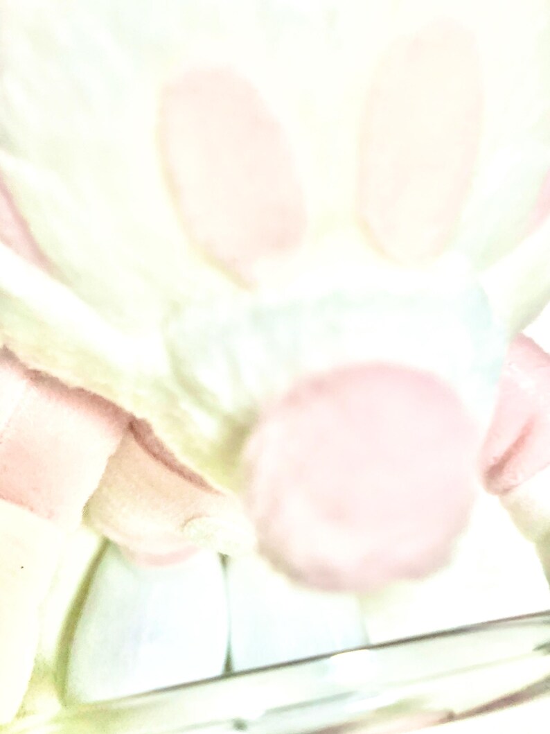 May include: A soft, plush toy featuring a rounded, light pink nose and pale, cream-colored fur. The character has two prominent, upright ears and a small, circular body structure. The overall appearance is light, airy, and brightly illuminated.
