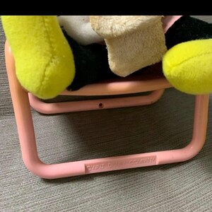 May include: A pink plastic chair with rounded corners, holding a plush toy with yellow, black, and beige elements. The text "WALT DISNEY COMPANY" is printed on the chair's frame. The toy's yellow hand and foot are visible.