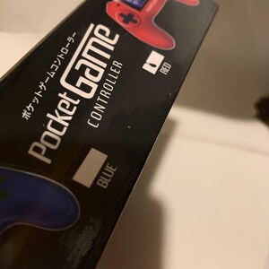 Pode incluir: Caixa preta para um Pocket Game Controller. A caixa apresenta um gr&aacute;fico de controlador vermelho e a palavra "RED" ao lado. A palavra "BLUE" tamb&eacute;m &eacute; vis&iacute;vel. Texto japon&ecirc;s tamb&eacute;m est&aacute; presente.