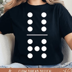 May include: Black t-shirt with a white domino design. The domino graphic has six white dots above a horizontal line and two white dots below. The text "GLOW THREAD DESIGN" is printed at the bottom of the image.