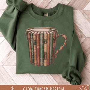 May include: A dark green sweatshirt with a unique design of a coffee mug constructed from books. The mug's handle has a twisted, multi-coloured pattern. The text "GLOW THREAD DESIGN" is displayed at the bottom of the image.