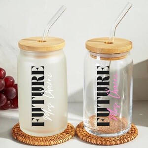 May include: Two glass tumblers with bamboo lids and glass straws. One tumbler is frosted, the other clear. Both feature the text "FUTURE Mrs. Chavez" in black and pink, respectively. They sit on woven coasters.
