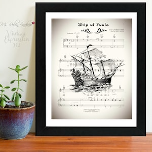 May include: Black framed print featuring sheet music with a detailed illustration of a sailing ship. The title "Ship of Fools" is displayed at the top, with the artist's name. The print has a vintage aesthetic, with the text "Vintage Expression 702" in the corner.