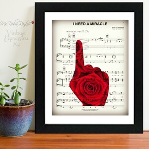 May include: A framed print of sheet music for the song "I Need a Miracle" by  Robert West. The sheet music features a red rose with a single finger pointing up.