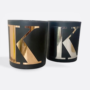 May include: Two black candle jars with the letter "K" in gold and silver foil on the front.