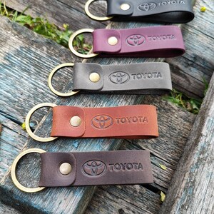 Pode incluir: Cinco chaveiros de couro em várias cores: preto, bordô, cinza, marrom e marrom escuro. Cada chaveiro apresenta um anel dourado e um fecho de pressão. O logotipo da Toyota e o nome da marca são gravados em relevo.