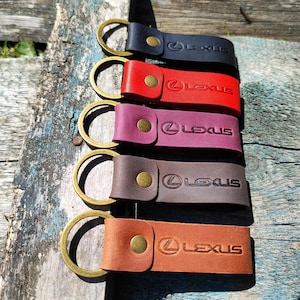 May include: Five leather keyrings in black, red, purple, brown, and tan. Each keyring has a gold-coloured ring and a snap closure. The word "LEXUS" is embossed on each keyring.