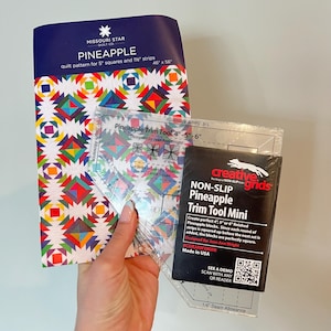 May include: A Missouri Star Quilt Co. Pineapple quilt pattern booklet for 5 inch squares and 1.5 inch strips, alongside a clear acrylic Creative Grids Pineapple Trim Tool Mini for 4, 5, or 6 inch finished blocks with printed instructions.