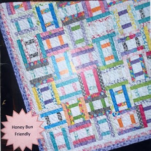 May include: A colorful quilt with a patchwork design. The quilt features a variety of fabrics in shades of blue, pink, orange, and green. The text "Criss Cross Applesauce" is displayed at the bottom, with "Sweet Jane's Quilting & Design" at the top.