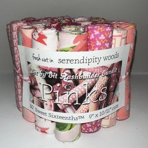 May include: A bundle of rolled fabric strips in various pink patterns. The bundle is wrapped with a label that reads "fresh cut in serendipity woods" and "Pinks." Each strip measures 9" x 10/11" and the bundle contains 30 cuts.