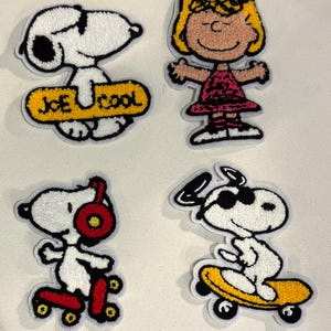 May include: Four embroidered patches featuring Peanuts characters. One patch shows Snoopy with the text "JOE COOL" on a yellow skateboard. Another shows Sally Brown. The other two show Snoopy skateboarding.