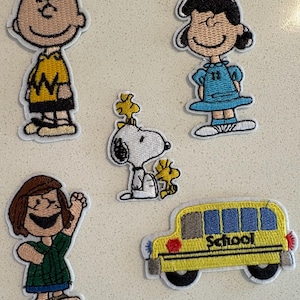 以下が含まれることがあります： ピーナッツのキャラクターが刺繍されたパッチ。 黄色のジグザグシャツを着たチャーリー・ブラウン、青いドレスを着たルーシー、ウッドストックとスヌーピー、緑のシャツを着た女の子、そして「School」という文字が入った黄色のスクールバスが含まれています。