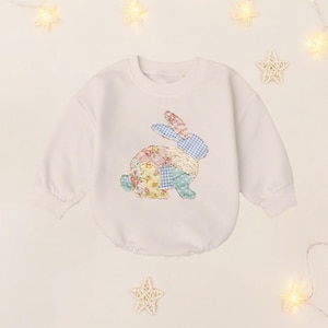 May include: White long-sleeved baby bodysuit with a patchwork bunny design. The bunny is made of floral, gingham, and lace fabrics in pastel colors. The bodysuit has a round neckline and long sleeves.
