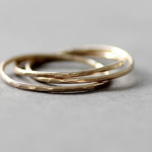 May include: Three gold hammered stacking rings. The rings are thin and delicate, and they are stacked on top of each other.