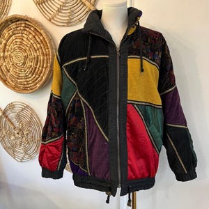 May include: A vintage patchwork jacket with a black corduroy center panel, gold trim, and a variety of colorful fabrics. The jacket features a zip-up front, a high collar, and a drawstring hem. The sleeves have a paisley pattern.
