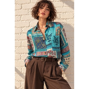 May include: A long-sleeved button-down shirt featuring a vibrant patchwork pattern in shades of teal, blue, red, and cream, paired with dark brown high-waisted trousers secured by a simple brown leather belt with a rectangular metal buckle.