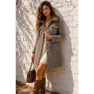 May include: A long-sleeved tweed coat featuring a brown and black checkered pattern, a faux fur collar, and front button closures. The coat is worn over a white lace dress and is paired with brown leather boots and a brown leather handbag.
