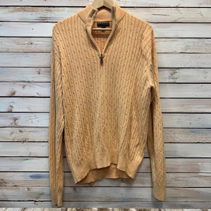May include: A light orange long-sleeve sweater featuring a cable knit pattern, a quarter-zip neckline with a metal zipper pull, and ribbed cuffs and hem. The interior collar tag displays the brand name Robert Talbott in black text.