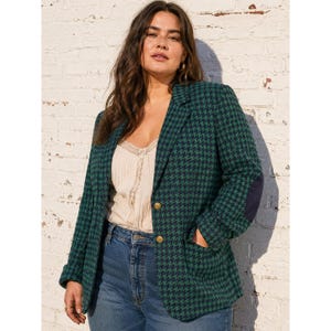 May include: A green and navy houndstooth blazer with gold buttons and a navy elbow patch. The blazer is paired with a cream-colored top and blue jeans. The blazer has a classic, tailored design.