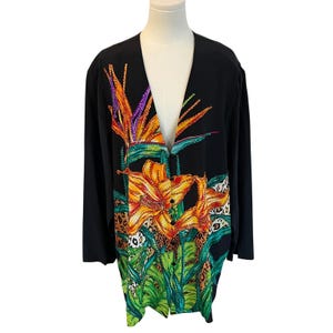 May include: Black long-sleeve button-up shirt with a vibrant floral print. The design features orange lilies, purple and orange bird of paradise flowers, and green foliage. The shirt has a V-neck and a leopard print accent.