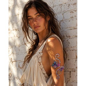 May include: A silver-toned metal arm cuff featuring a swirling wire design adorned with small, multi-colored floral accents in shades of blue, purple, and pink. The piece is worn on the upper arm, showcasing intricate metalwork and colorful details.