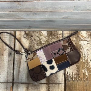 May include: A patchwork clutch with a brown leather wrist strap. The rectangular bag features a variety of fabrics in shades of brown, tan, purple, and black, including a section of cowhide with black spots. The bag has a zipper closure.