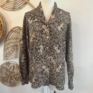 Puede incluir: Camisa de manga larga con estampado de animal print marrón y beige. La camisa se exhibe en un maniquí. Tiene cuello y se abrocha con botones en la parte delantera.