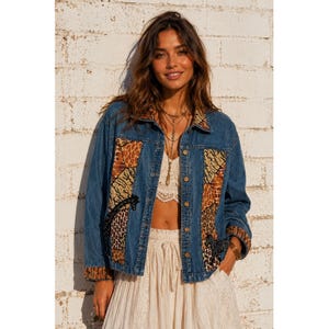 May include: A blue denim jacket featuring long sleeves, a collar, and front button closures. The jacket is accented with panels of brown and black animal print patterns on the front and cuffs, along with black embroidered giraffe motifs.