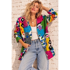 May include: A long-sleeve blazer featuring a vibrant, multi-coloured patchwork pattern with geometric shapes, floral motifs, and polka dots in shades of blue, yellow, green, pink, and black, finished with a black and white striped trim along the front.