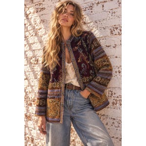 May include: A long-sleeve open-front jacket featuring a multi-coloured tapestry pattern in shades of deep purple, gold, and blue. The garment has a structured collarless neckline, a button-down front placket, and a textured fabric finish.
