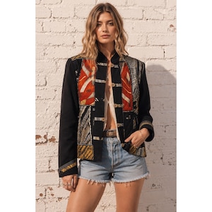 Puede incluir: Una chaqueta negra con un diseño de patchwork en los paneles frontales, con secciones de tela estampada en naranja, amarillo y gris. La chaqueta tiene mangas largas, cuello mao y cierre frontal con botones pequeños, combinada con pantalones cortos de mezclilla azul.