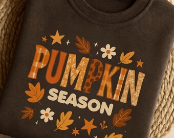 May include: Dark brown sweatshirt with the words "PUMPKIN SEASON" in orange and white lettering. The letters have plaid and floral patterns. The design includes fall leaves, stars, and flowers.