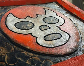 May include: A wooden sign with a red frame and a black and white skull design painted on it. The skull is surrounded by a red circle and the background is black with a pattern of circles.