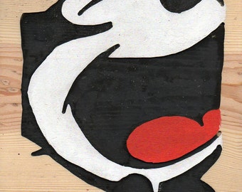 May include: A black and white cartoon character with a large, open mouth and a red tongue. The character is painted on a wooden surface.
