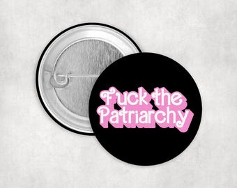 May include: A black button with the phrase "Fuck the Patriarchy" in pink and white bubble letters. The button is round with a metal pin back.