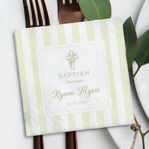 May include: A square paper napkin featuring a light green and white vertical striped pattern. The center displays a white square with a cross graphic, floral accents, and the text BAPTISM, Ryann Myers, and the date 08.20.2026 in green ink.