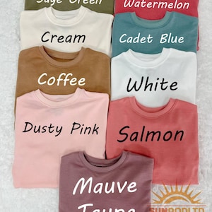 May include: A collection of crewneck sweatshirts in various colors, including sage green, cream, coffee, dusty pink, watermelon, cadet blue, white, salmon, and mauve taupe. Each sweatshirt has the color name printed on it in a bold, black font.