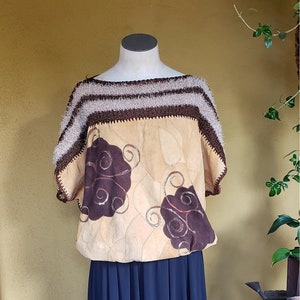 May include: A beige crochet top with brown and white stripes, featuring a brown floral design. The top is paired with a dark blue skirt.