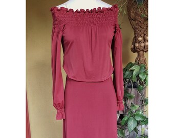 May include: A long, burgundy off-the-shoulder dress with long sleeves and a gathered neckline. The dress has a fitted bodice and a flowing skirt.
