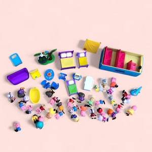 May include: A collection of plastic toy figures and miniature furniture pieces, including beds, a yellow bathtub, a blue bus, and various cartoon animal characters in diverse colours, arranged on a solid light pink surface for play.