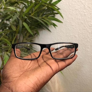 May include: A pair of rectangular eyeglasses with a solid black frame and clear lenses. The frames feature a classic design with a straight bridge and thin temples, providing a clean and functional look for everyday vision correction needs.