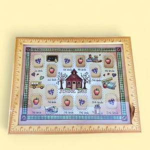Peut inclure: Cadre photo en bois avec bordure de règle, présentant un design sur le thème de l'école. Le cadre comprend des espaces pour les photos, avec des illustrations de pommes, de cœurs, d'un bus scolaire et d'une école. Les mots "School Days" sont affichés.