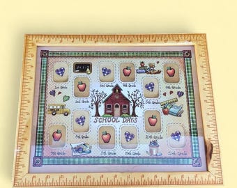 Könnte beinhalten: Ein Holzbilderrahmen mit Linealrand, der ein Design zum Thema Schule aufweist. Der Rahmen enthält Platz für Fotos mit Illustrationen von Äpfeln, Herzen, einem Schulbus und einem Schulhaus. Die Worte "School Days" sind deutlich sichtbar.
