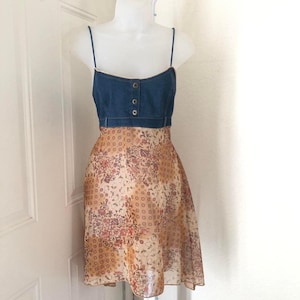 Könnte beinhalten: Ein Kleid mit einem Jeans-Oberteil und einem Rock mit Blumenmuster. Das Oberteil hat dünne Träger und drei Knöpfe. Der Rock hat ein Muster aus kleinen Quadraten und floralen Designs in Braun-, Pfirsich- und Cremetönen.