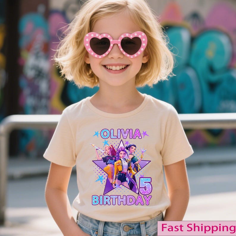 Puede incluir: Camiseta beige con un gr&aacute;fico de estrella y el texto "OLIVIA BIRTHDAY 5". El gr&aacute;fico presenta personajes de dibujos animados en varios colores. La persona de la imagen lleva gafas de sol rosas en forma de coraz&oacute;n.