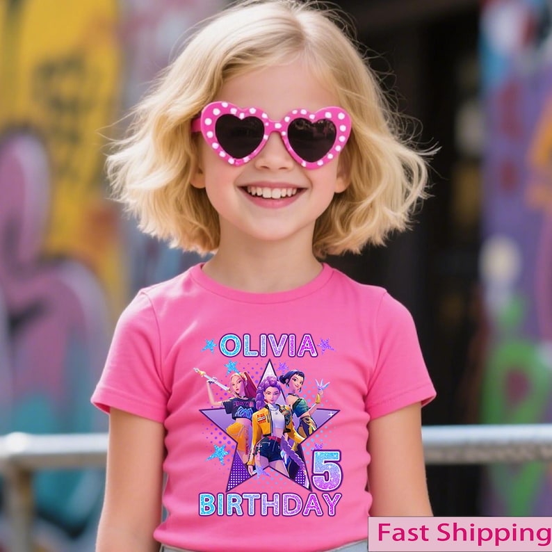 Puede incluir: Una ni&ntilde;a peque&ntilde;a con gafas de sol rosas en forma de coraz&oacute;n con lunares blancos y una camiseta rosa. La camiseta presenta el nombre "Olivia", un gr&aacute;fico de tres personajes, el n&uacute;mero "5" y la palabra "Cumplea&ntilde;os".