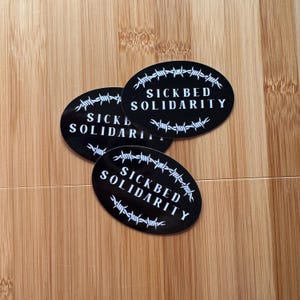 three SICKBED SOLIDARITY | black and white, barbed wire, oval sticker on wood