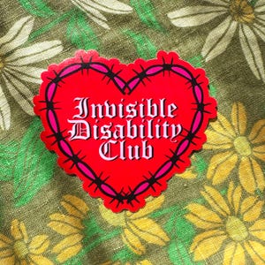 May include: A red heart-shaped sticker with the text "Invisible Disability Club" in a gothic font. The heart is outlined with pink and black barbed wire. The sticker is on a floral background.