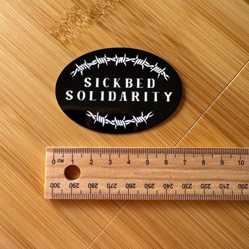SICKBED SOLIDARITY | black and white, barbed wire, oval sticker on wood with ruler below showing 72mm width